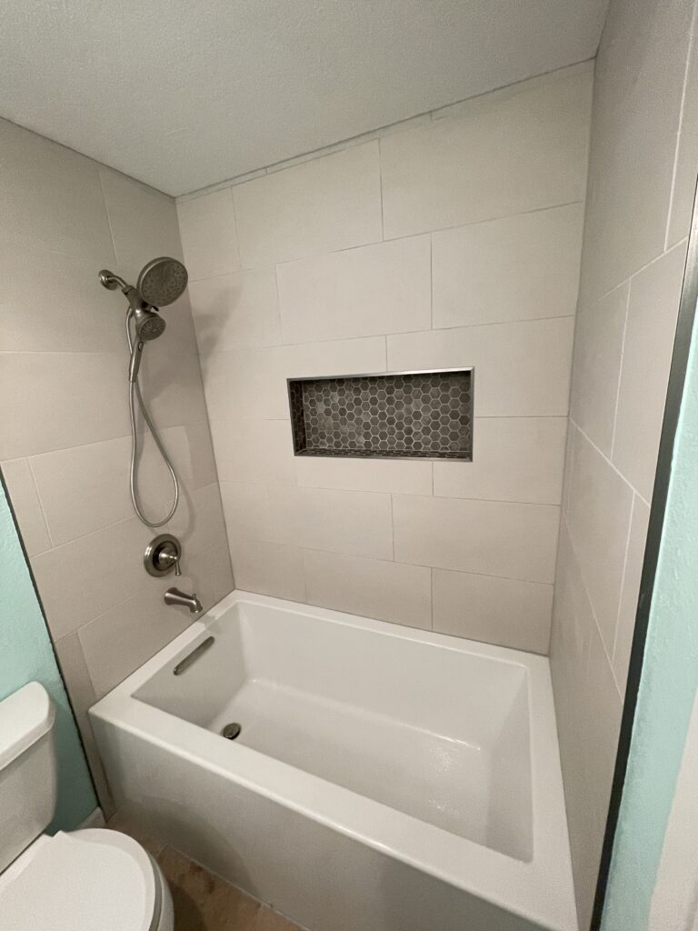 Modern spacious bathtub with a niche installed on the wall and a brand new shower head.